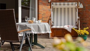 Un patio con una mesa preparada para dos, una silla lounge a rayas y una maceta con flores amarillas.