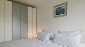 Un dormitorio con cama, almohadas, una mesita de noche, lámpara, armario y un cuadro en la pared.