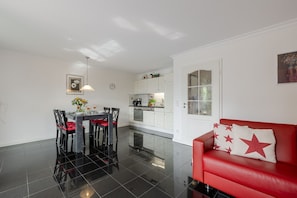 Una cocina moderna con armarios blancos, una mesa de comedor con sillas y un sofá rojo con almohadones de estrellas.