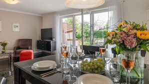 Un moderno comedor con una mesa de vidrio dispuesta para una comida, un televisor al fondo y vistas al exterior a través de amplios ventanales.