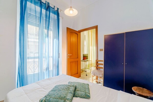 Un dormitorio con cama, armario, silla y escritorio con computadora.