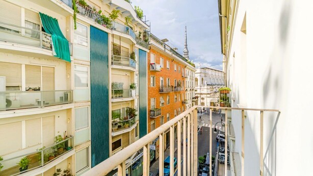 Un edificio a più piani con balconi, una strada sottostante e una torre sullo sfondo.