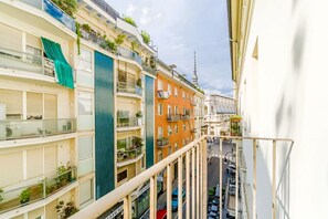 Un edificio de varios pisos con balcones, una calle abajo y una torre al fondo.