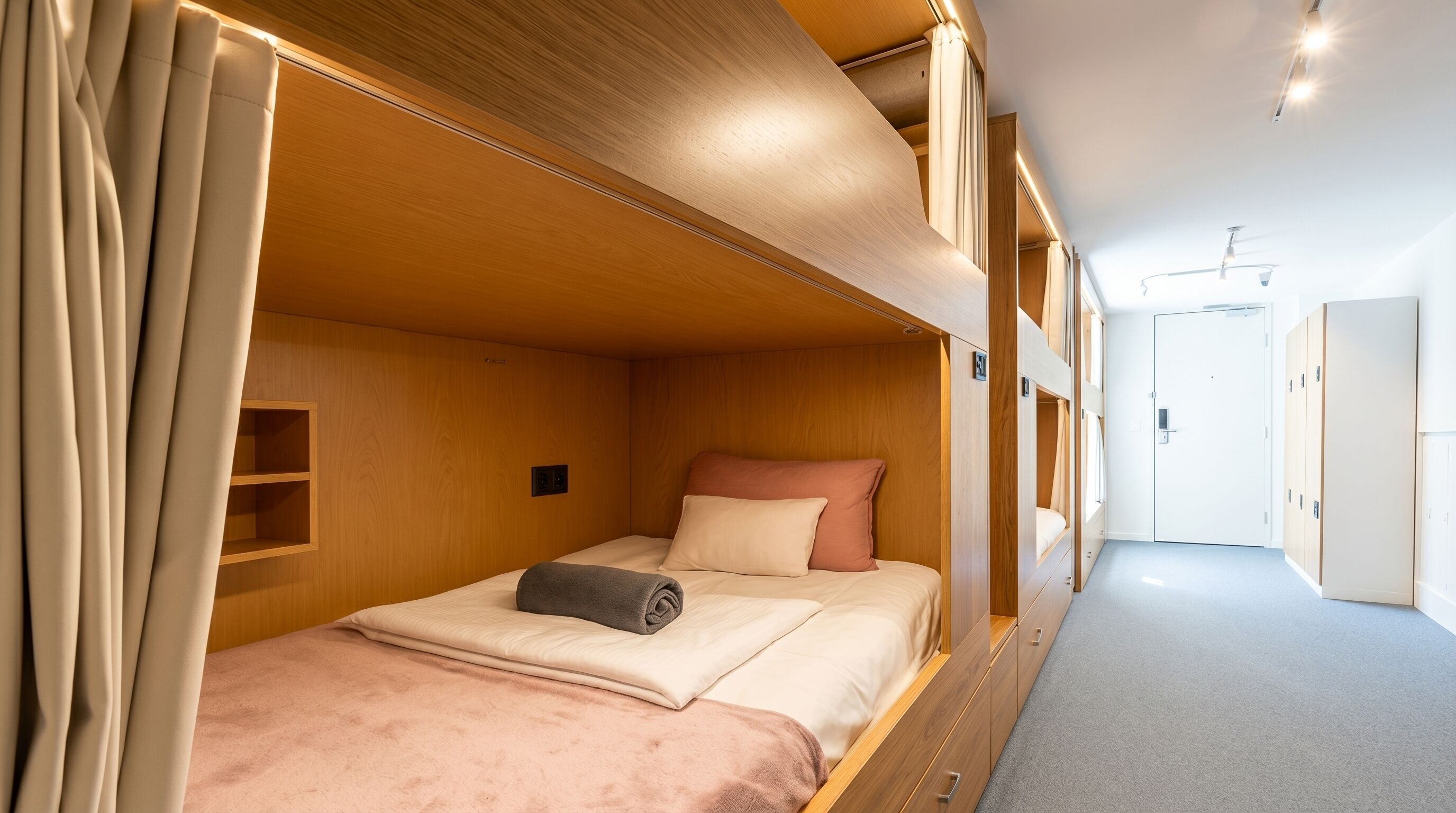 A compact, well-lit room with a bunk bed, a small shelf, and a door leading to another area.