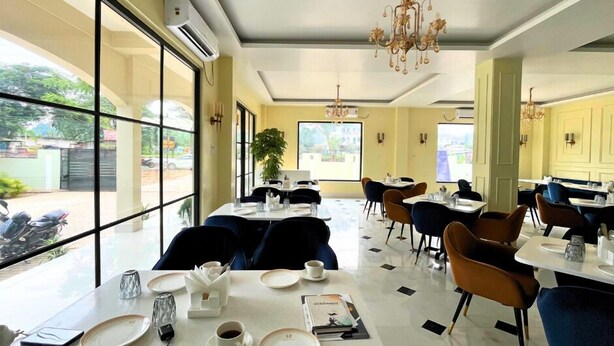 A restaurant with tables and chairs, a chandelier, and large windows. - Hatimurias Boutique Resort (Sonapur)