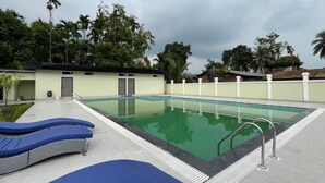 A swimming pool with lounge chairs, a covered area, and a building with doors and windows. - Hatimurias Boutique Resort (Sonapur)