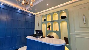 A reception desk with a laptop, a nameplate, and a chandelier. - Hatimurias Boutique Resort (Sonapur)
