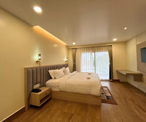 A modern hotel room with a large bed, bedside tables, a TV, and a view of the outdoors.