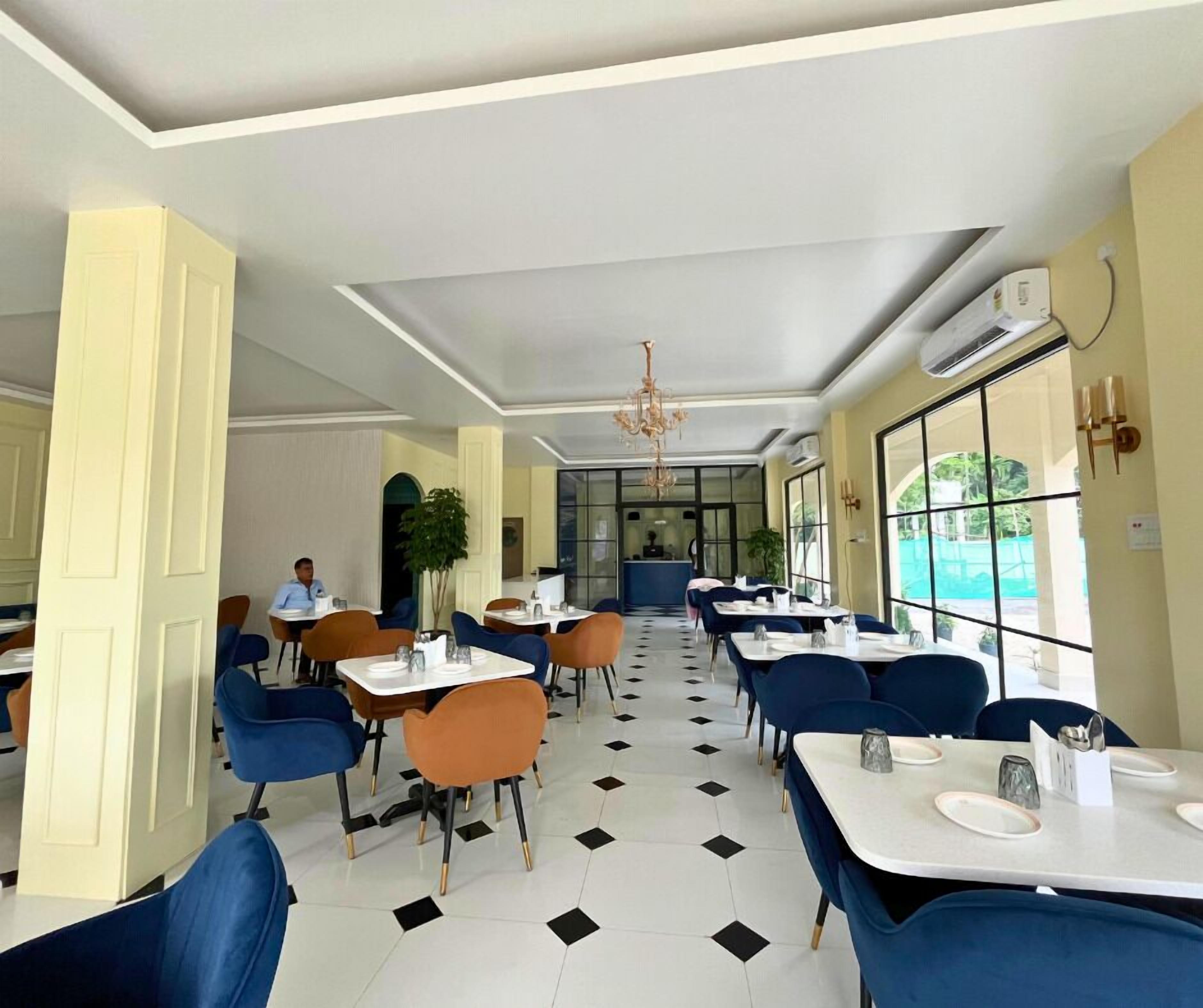 A restaurant with a checkered floor, blue and orange chairs, and a chandelier.
