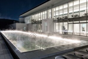 A modern building with a large glass facade, a water feature in the foreground, and outdoor seating visible through the windows. - UniIsland The SpaVille (Incheon)