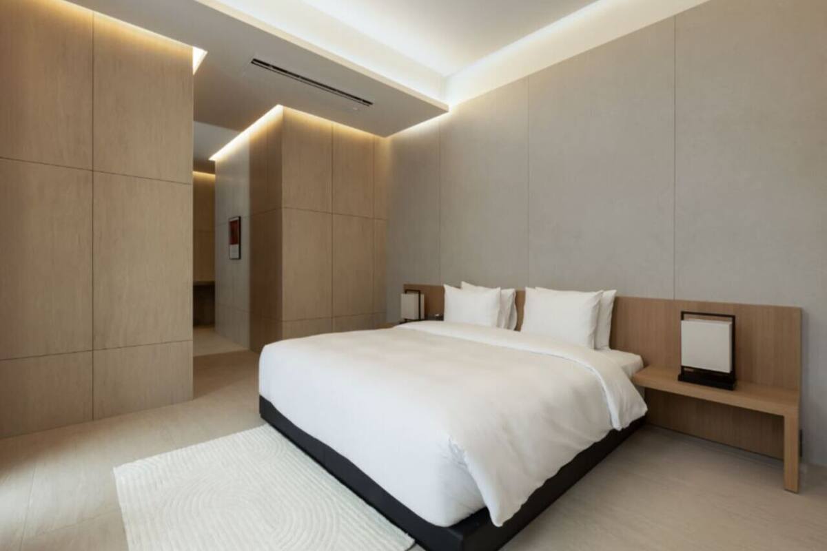 A modern hotel room with a large bed, built-in storage, and a minimalist design.