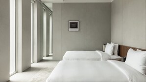 Habitación de hotel moderna con dos camas, un cuadro enmarcado en la pared y ventanas grandes que dejan entrar luz natural.