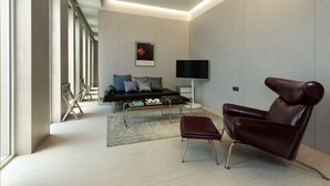 Una sala de estar moderna con un sofá, un sillón de cuero, un televisor de pantalla plana y un ventanal grande.
