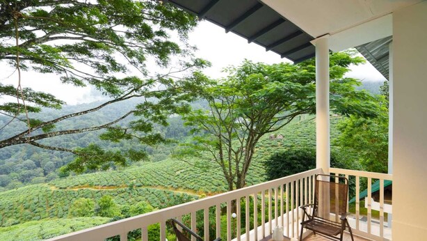 A balcony with a view of a lush green landscape, a table with chairs, and a white railing.