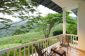 A balcony with a view of a lush green landscape, a table with chairs, and a white railing.