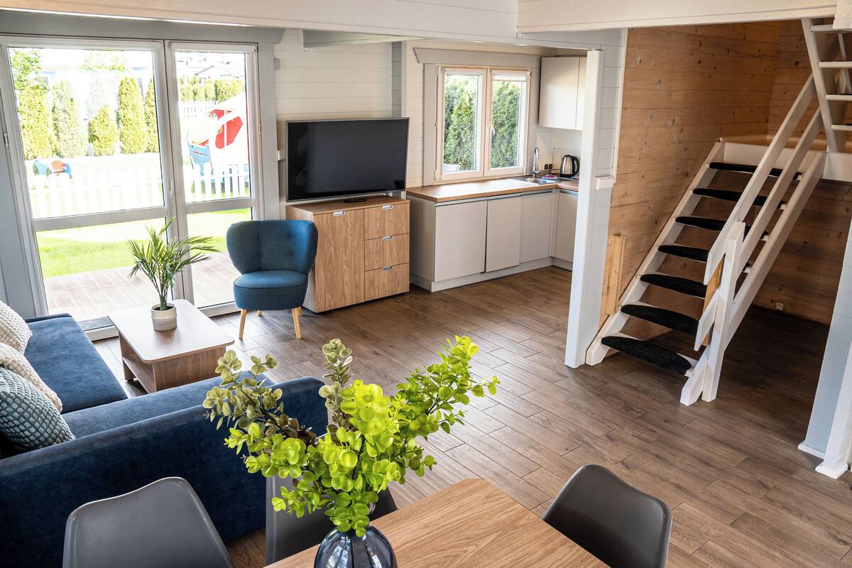 Un espacio habitable compacto con sofá, mesa de comedor, televisor, zona de cocina y escalera.