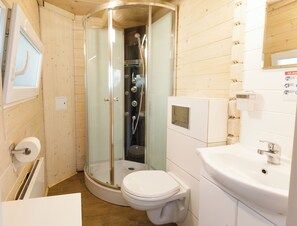 Ett litet badrum med träinredning, en dusch med glasväggar, en toalett och ett handfat.