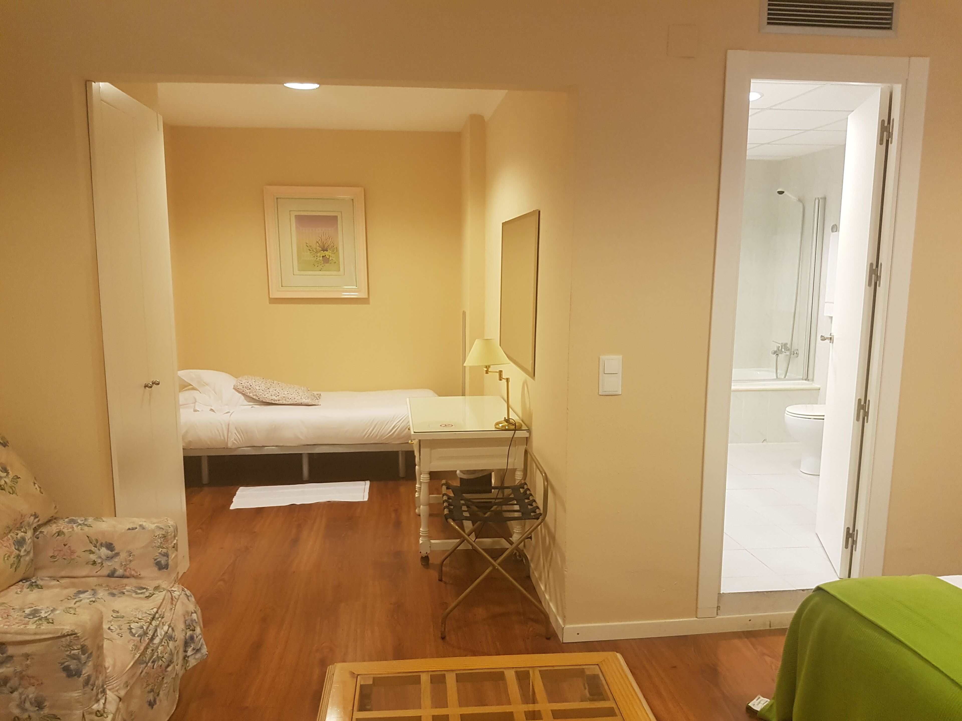 A bedroom with a bed, bedside table, lamp, and a small desk with a chair.