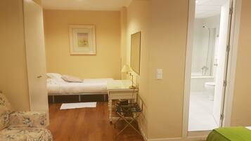 A bedroom with a bed, bedside table, lamp, and a small desk with a chair.