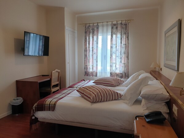 A hotel room with a bed, a desk, a chair, a TV, a window with curtains, and a phone on the desk. - HOTEL DEL CARME (Vilagrasa)