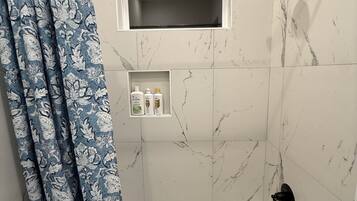 Un baño con bañera, ducha, una ventana y un estante con artículos de aseo.