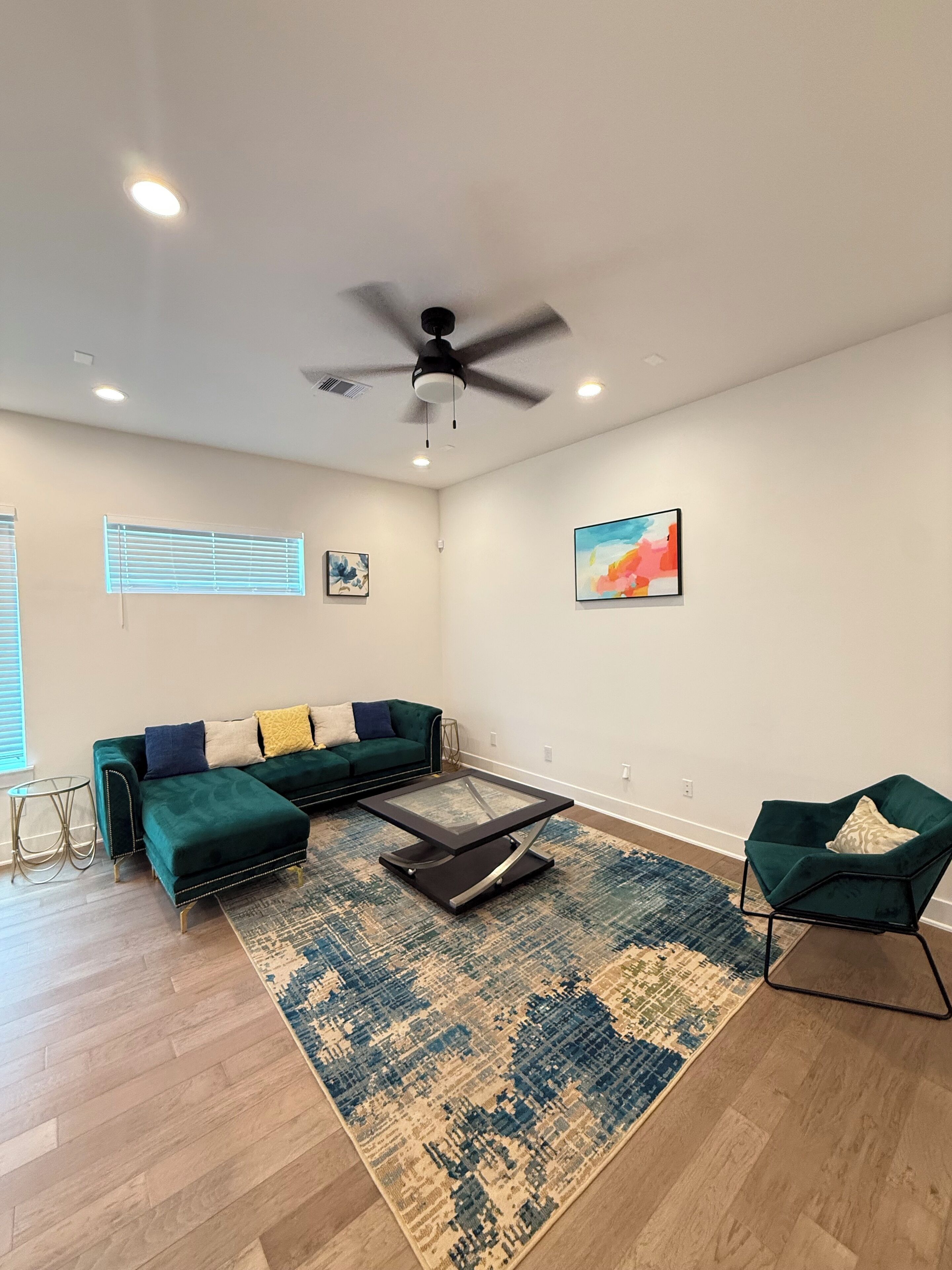 A modern living room with a sectional sofa, a glass coffee table, a green armchair, and a ceiling fan.