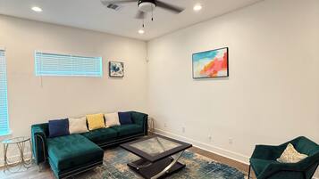 A modern living room with a sectional sofa, a glass coffee table, a green armchair, and a ceiling fan.