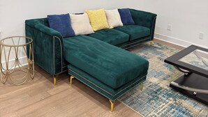 Un salon avec un canapé d’angle turquoise, une table d’appoint dorée et un tapis à motifs.