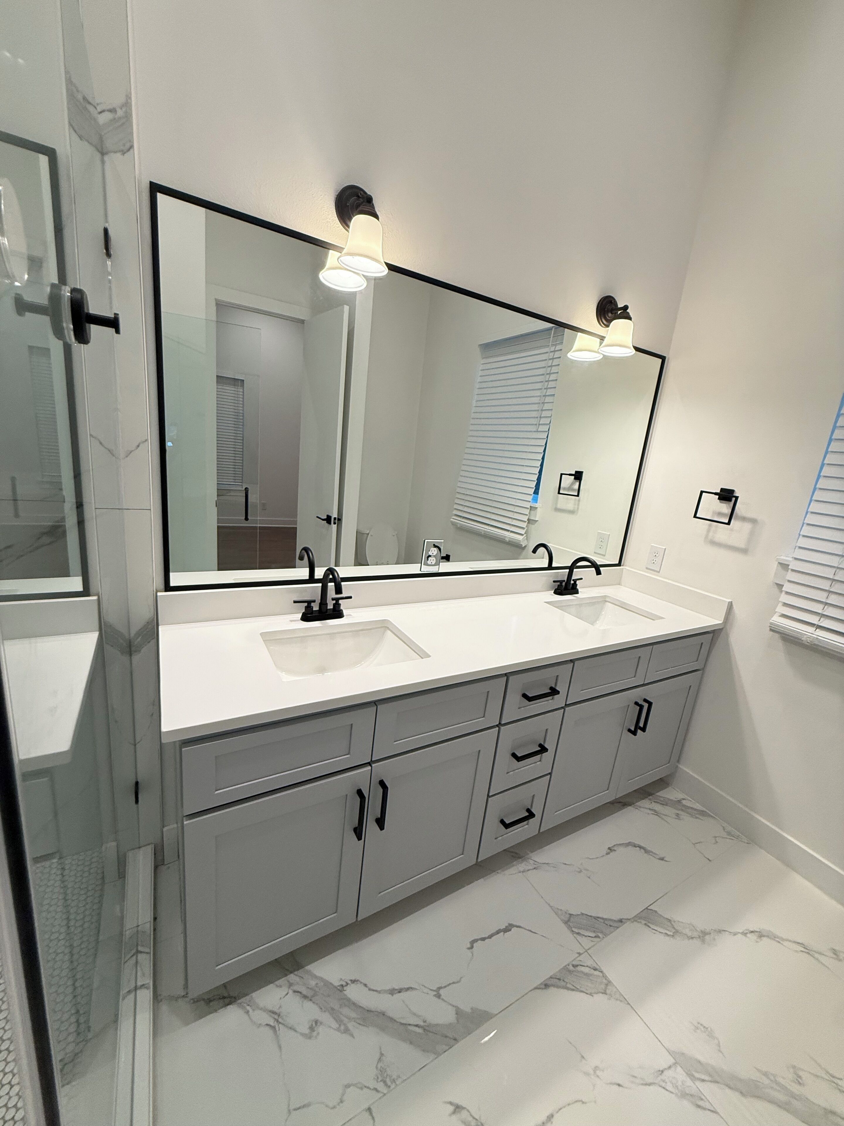 A bathroom with a double sink vanity, a large mirror, and a glass shower enclosure.