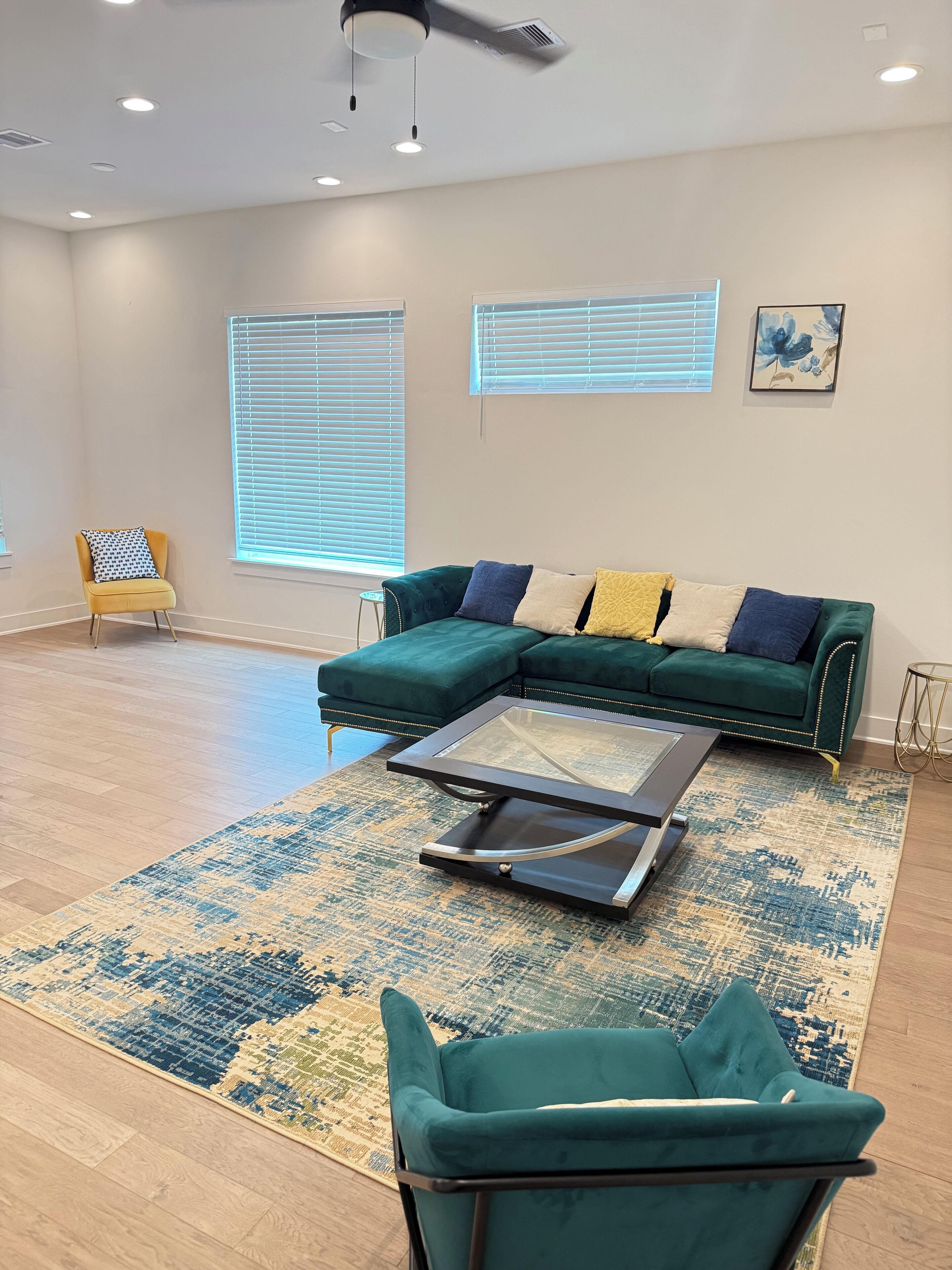 Ein modernes Wohnzimmer mit einem Ecksofa, einem Glastisch und einem Türkis-farbenen Sessel.