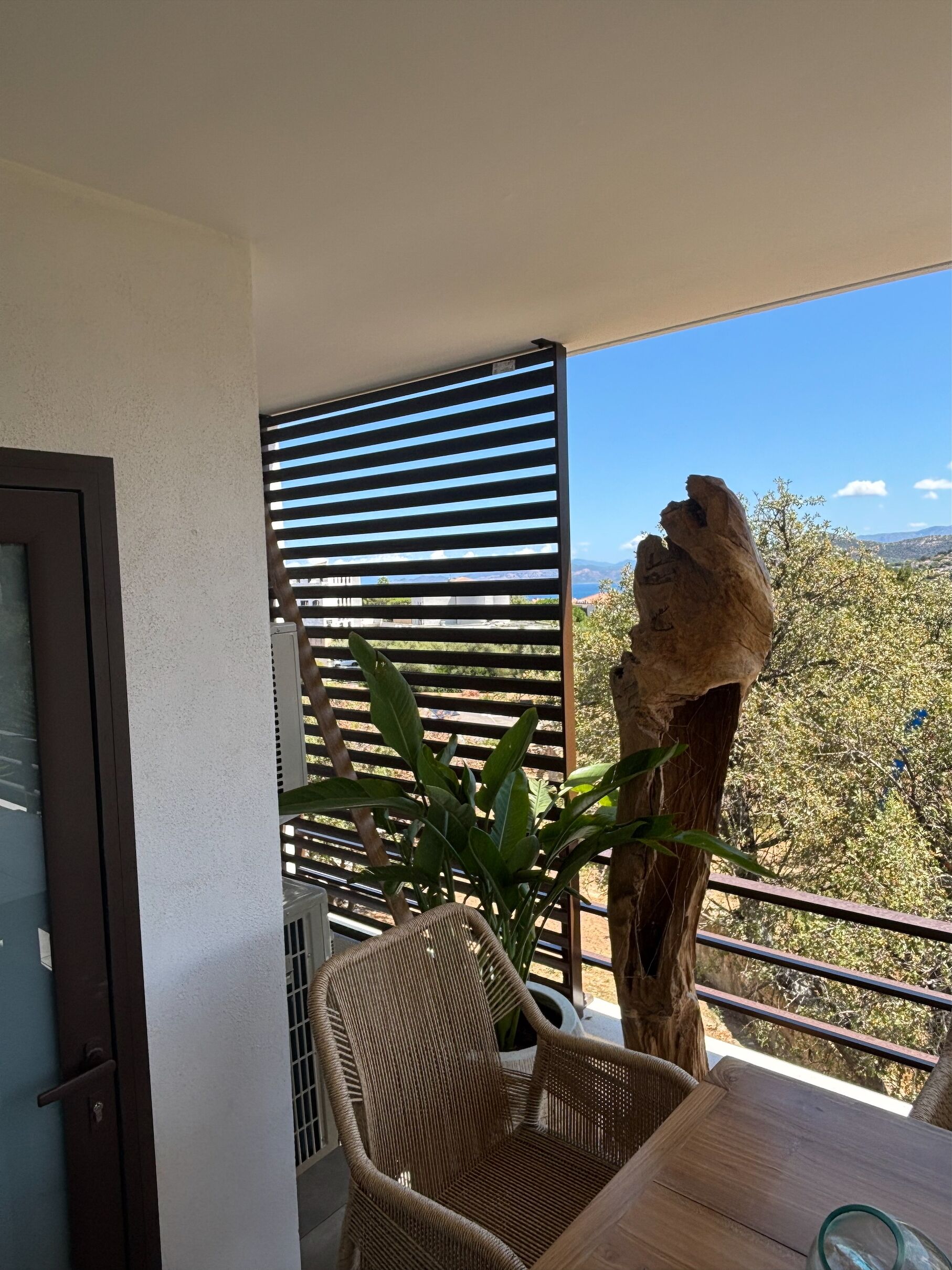 A balcony with a wicker chair, a wooden table, and a view of the landscape.
