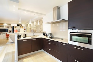Una cocina moderna con armarios oscuros, horno empotrado e iluminación colgante.