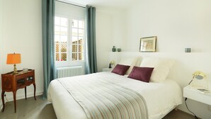 Ein Schlafzimmer mit einem Bett, einem Nachttisch, einer Lampe, einem Fenster mit Vorhängen und einem Wandbild.