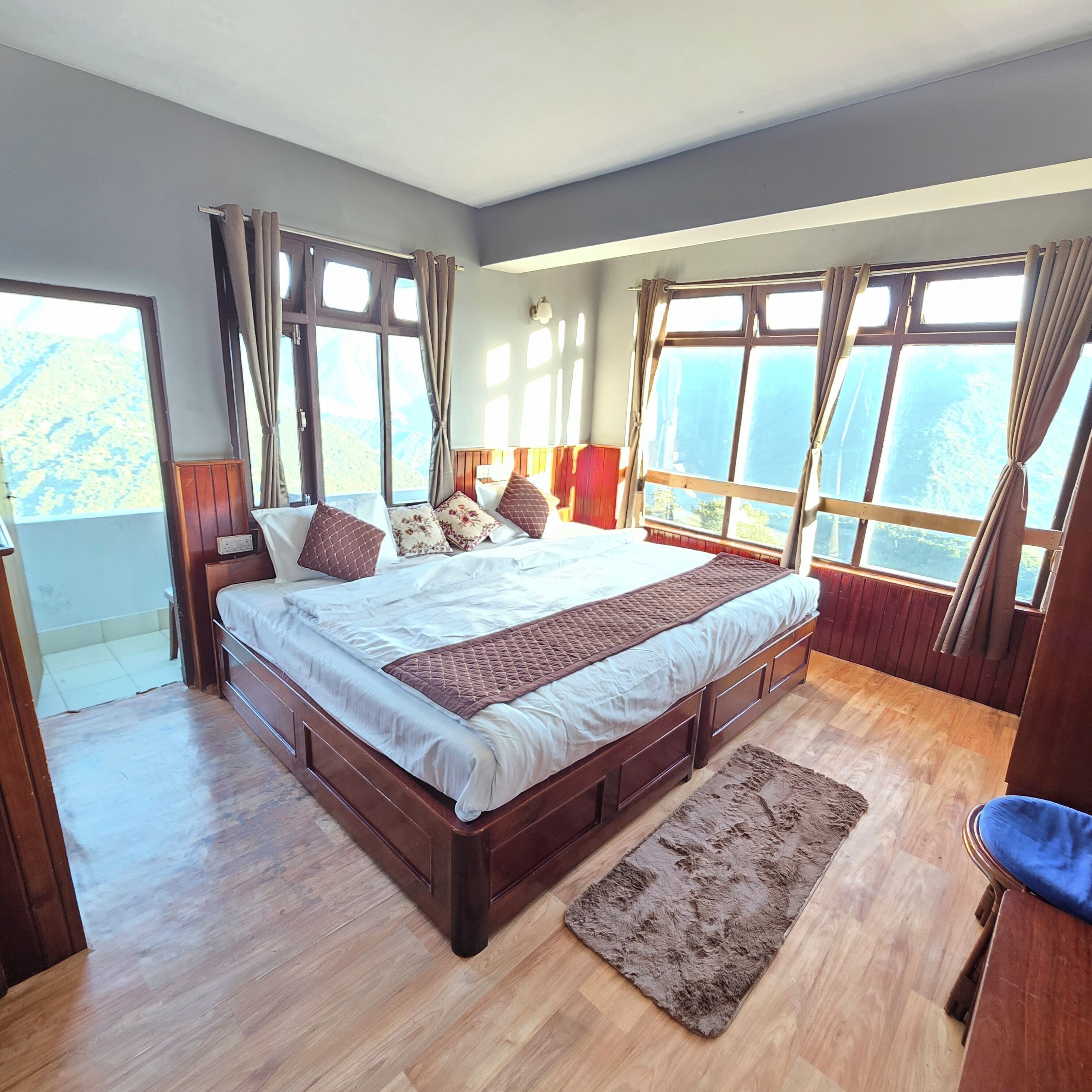 A large bed with a wooden frame, a fluffy rug, and curtains on a window with a view of the outdoors.