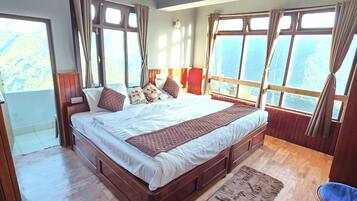 A large bed with a wooden frame, a fluffy rug, and curtains on a window with a view of the outdoors.