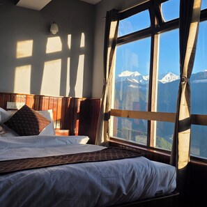 A bedroom with a large window overlooking a mountain range.