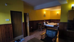 Una habitación con paredes y suelos de madera, una cama con ropa blanca, un escritorio, una silla y una pequeña mesa.
