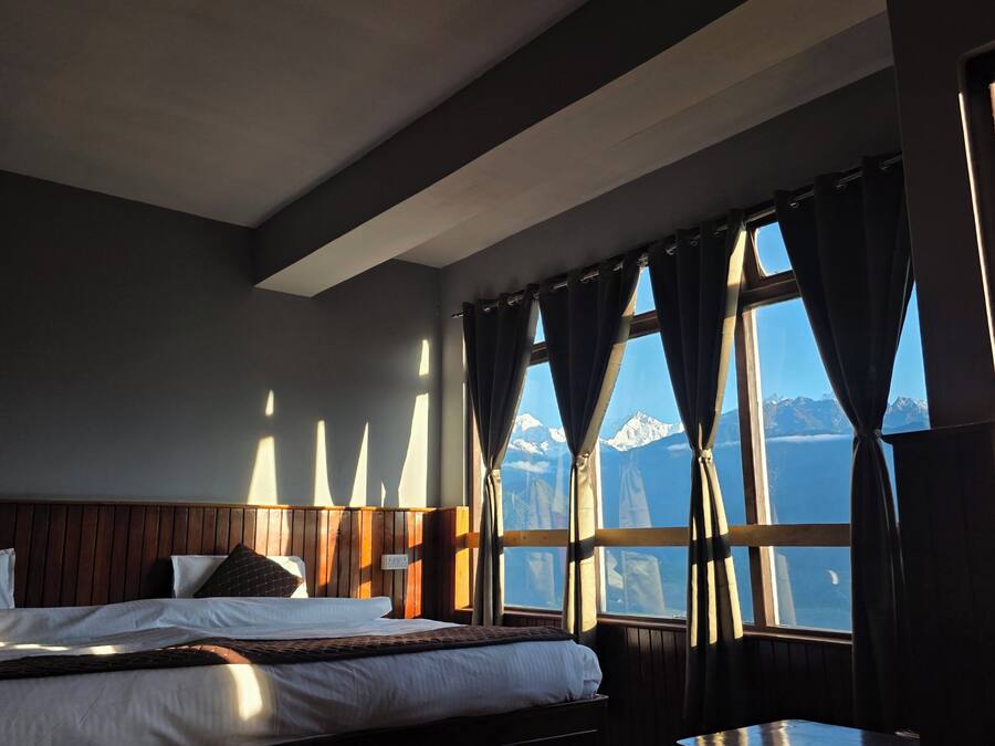 A hotel room with a bed, a wooden headboard, a window with curtains, and a view of mountains.
