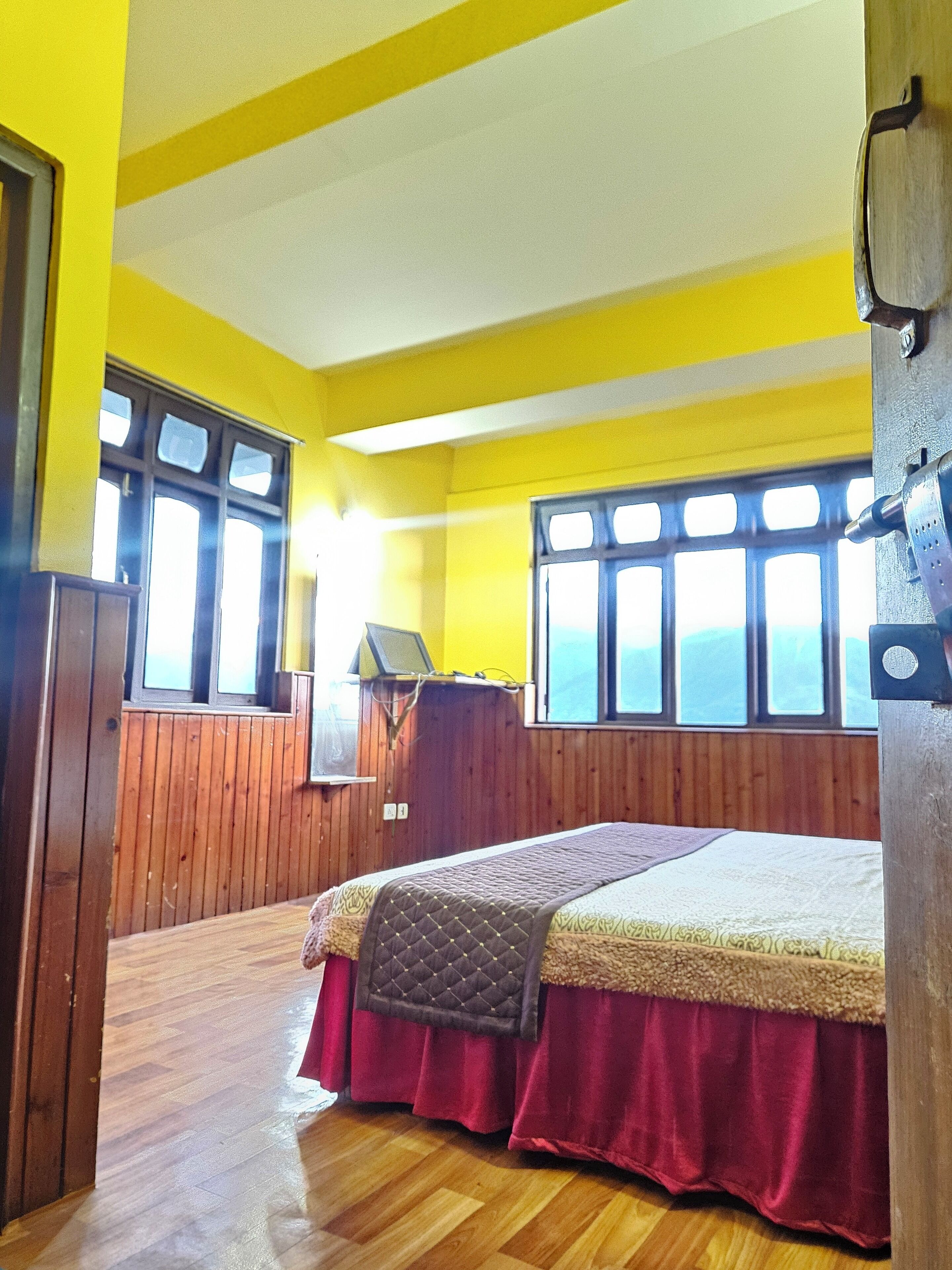 Una habitación con piso de madera, una cama con colcha roja y beige, y paredes amarillas.