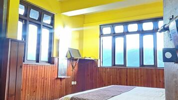 Una habitación con piso de madera, una cama con colcha roja y beige, y paredes amarillas.