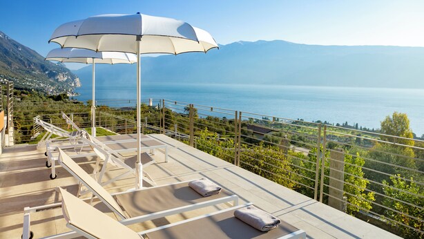 A terrace with sun loungers and umbrellas overlooking a coastal landscape. - Relais Zenner (Toscolano Maderno)