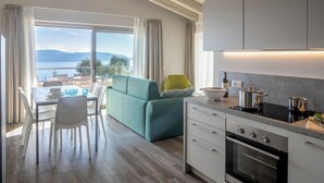 A modern kitchen with a dining area, a sofa, and a view of the lake. - Relais Zenner (Toscolano Maderno)