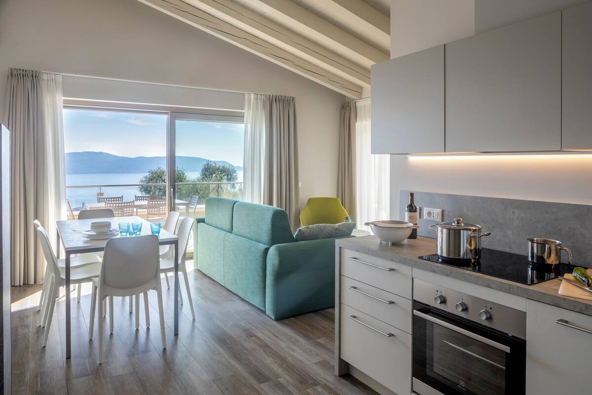 A modern kitchen with a dining area, a sofa, and a view of the lake.