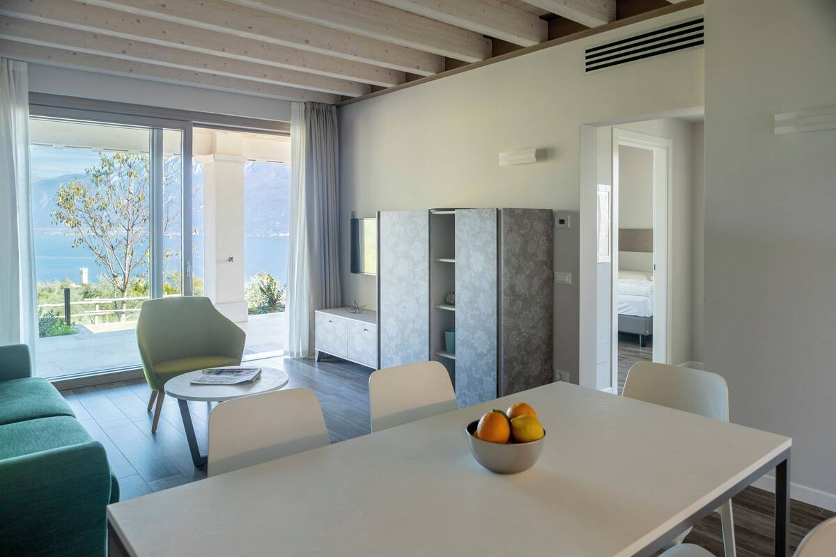 A modern hotel room with a balcony, a dining area, and a TV.