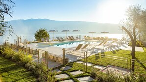 A pool area with lounge chairs and umbrellas, surrounded by a wooden fence and greenery. - Relais Zenner (Toscolano Maderno)