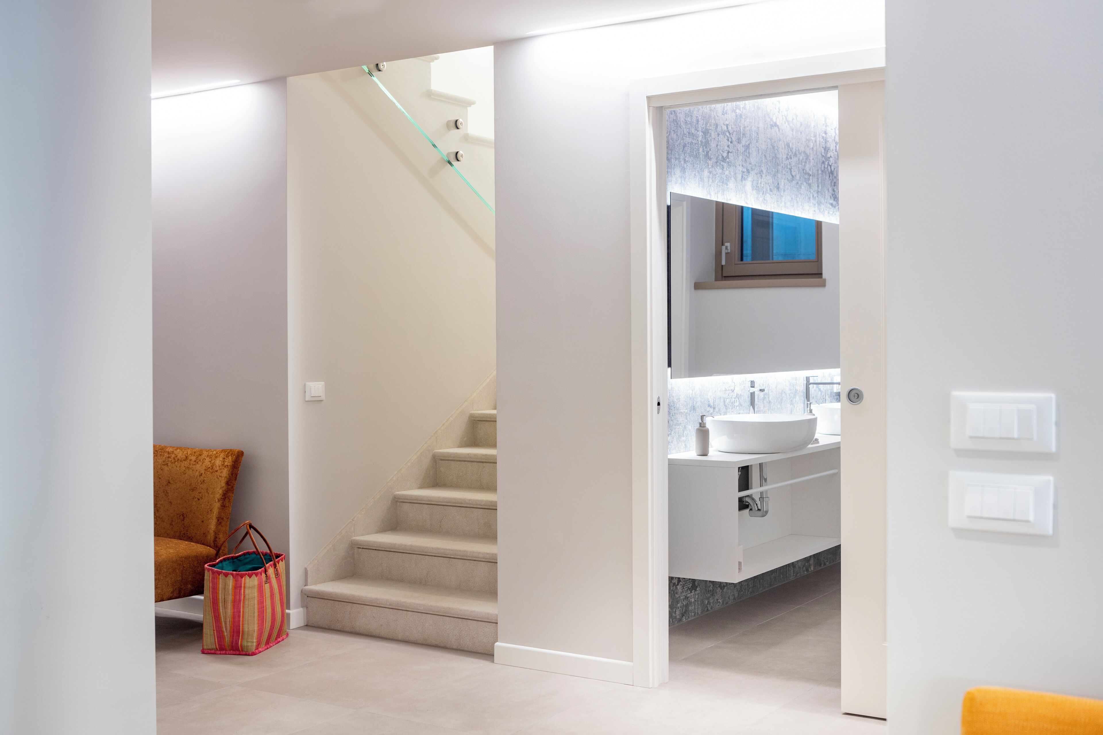 A modern bathroom with a white sink, a mirror above it, and a window with a view of trees.