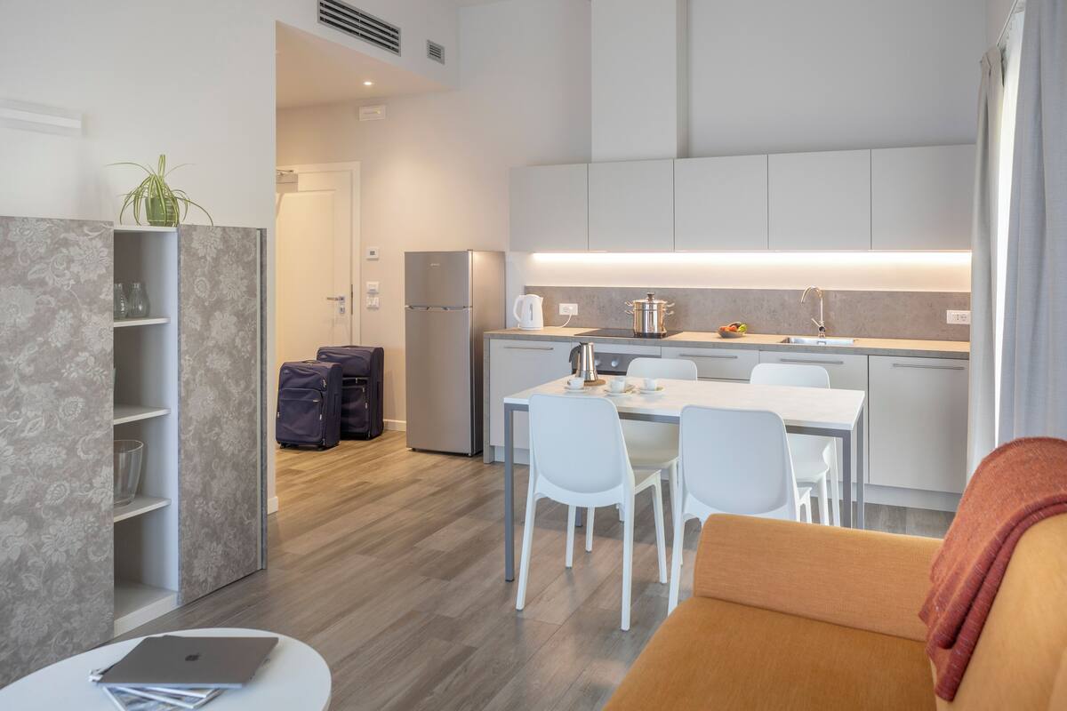 A modern kitchen with a dining area, a sofa, and a laptop on a table.