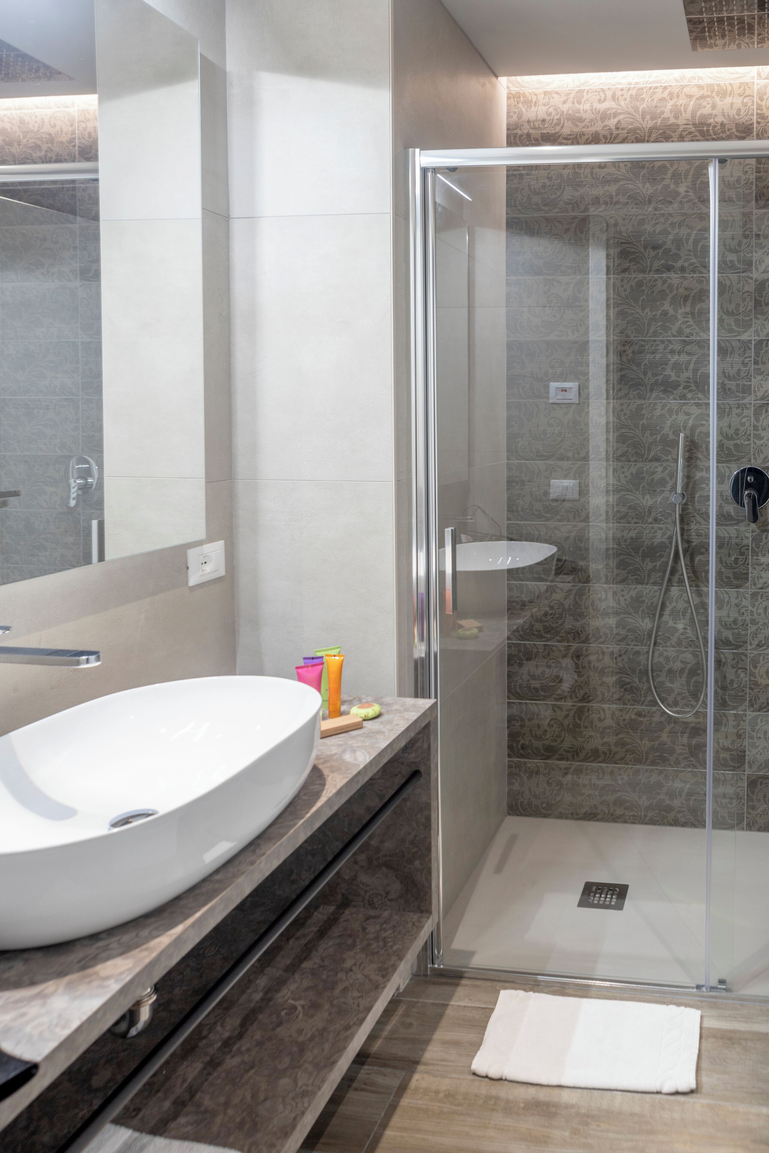 Ein modernes Badezimmer mit einer gläsernen Duschkabine, einem weißen Waschbecken und einem Spiegel.
