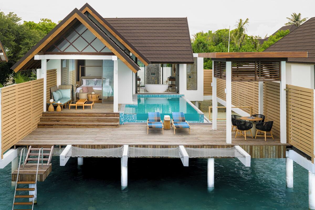 En modern villa byggd på pålar över vattnet, med en pool, ett trädäck och en loungehörna.