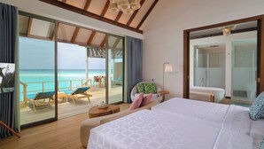 A hotel room with a large bed, a glass door leading to a balcony with a view of the ocean, a small table, and a chair. - Meyyafushi Maldives - Premium All Inclusive (Meyyafushi)